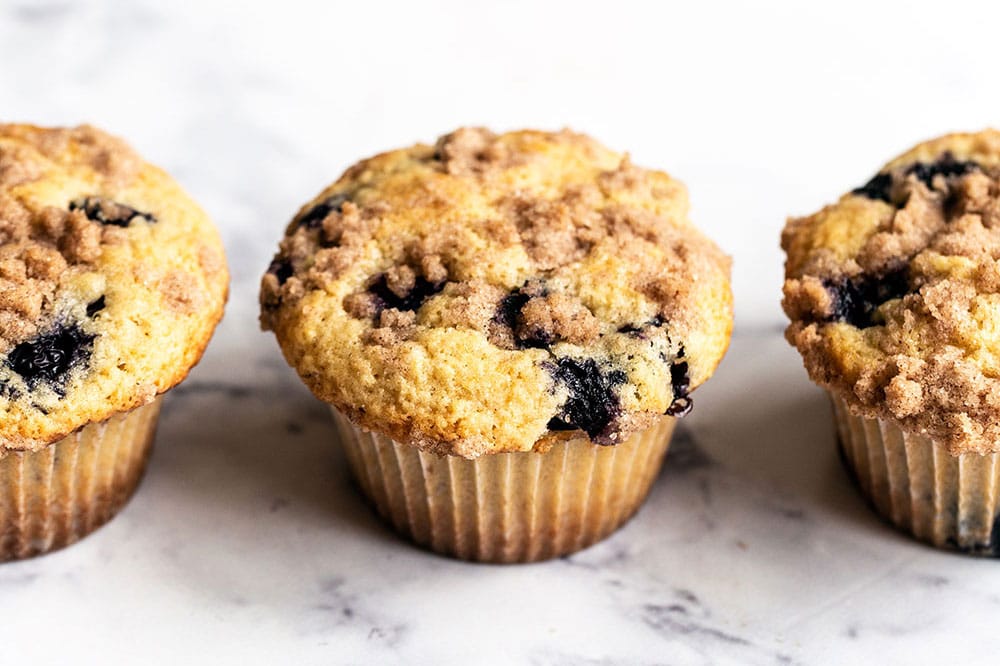 Drie zelfgemaakte bosbes muffins, verrijkt met bruine boter en afgewerkt met een krokante crumb topping.