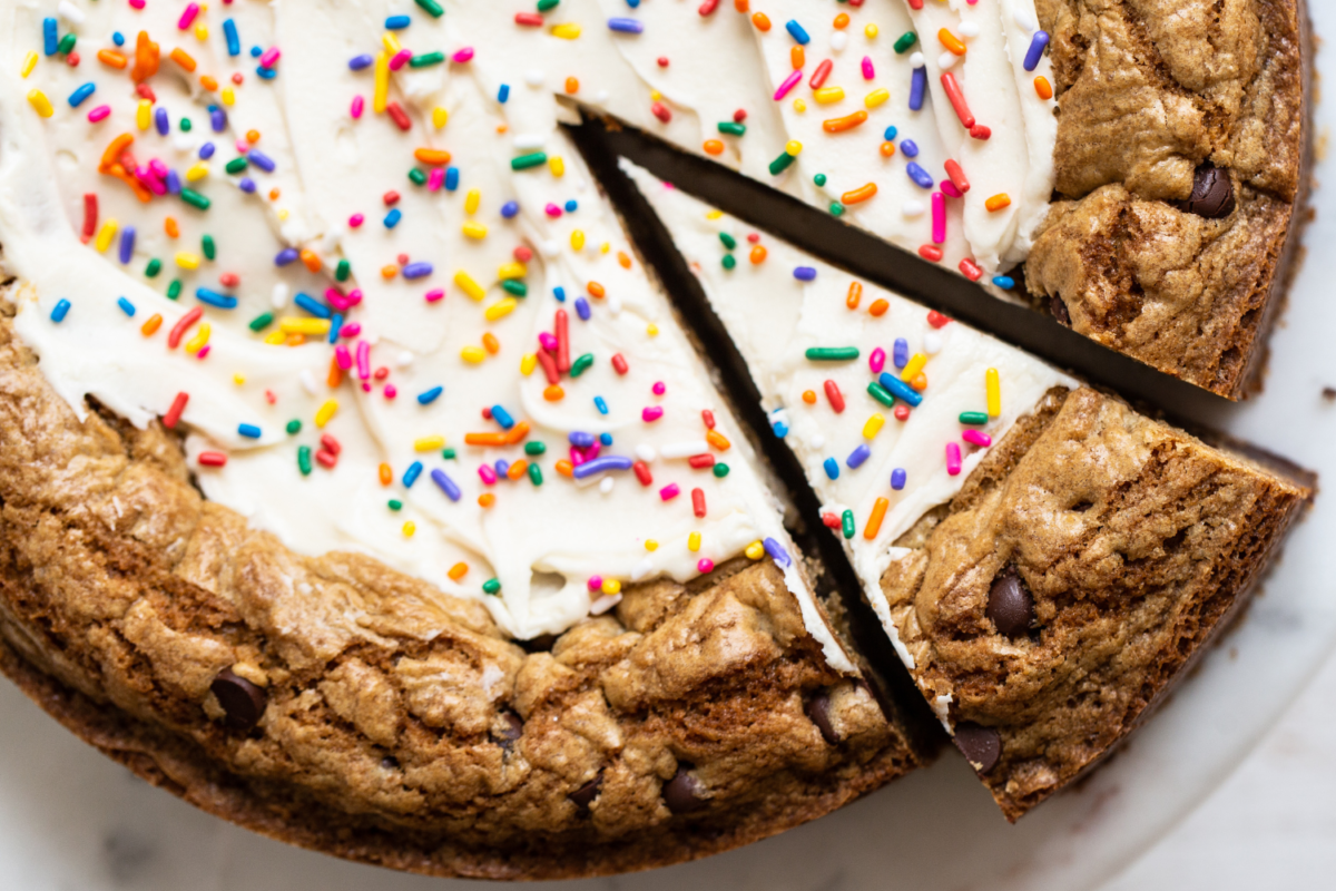 Chocolate chip cookie cake met romige witte glazuur en regenboogsprinkles, met een stuk dat wordt gesneden om te serveren