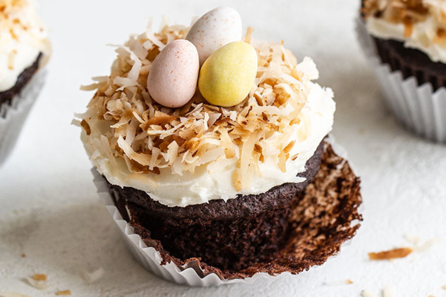 Chocolade cupcake met kokosfrosting, gegarneerd met geroosterde kokos en chocolade-eitjes, met het papiertje half verwijderd, klaar om van te genieten