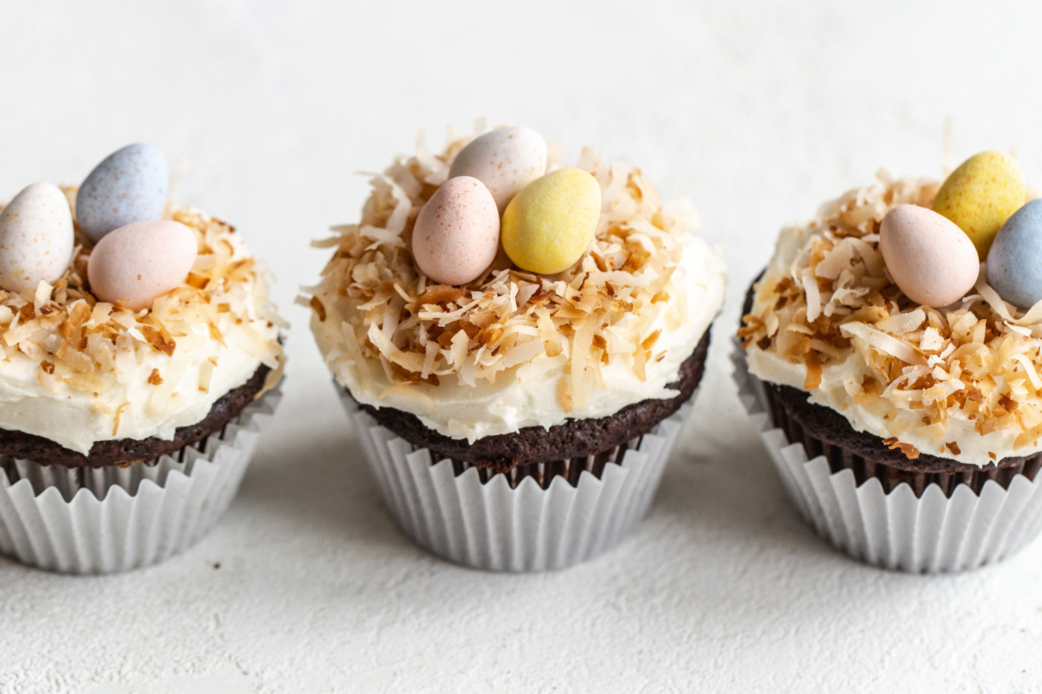 Drie afgewerkte chocolade-kokoscupcakes op een rij, gegarneerd met kokosvlokken en klaar om te serveren als een heerlijke zoete traktatie.