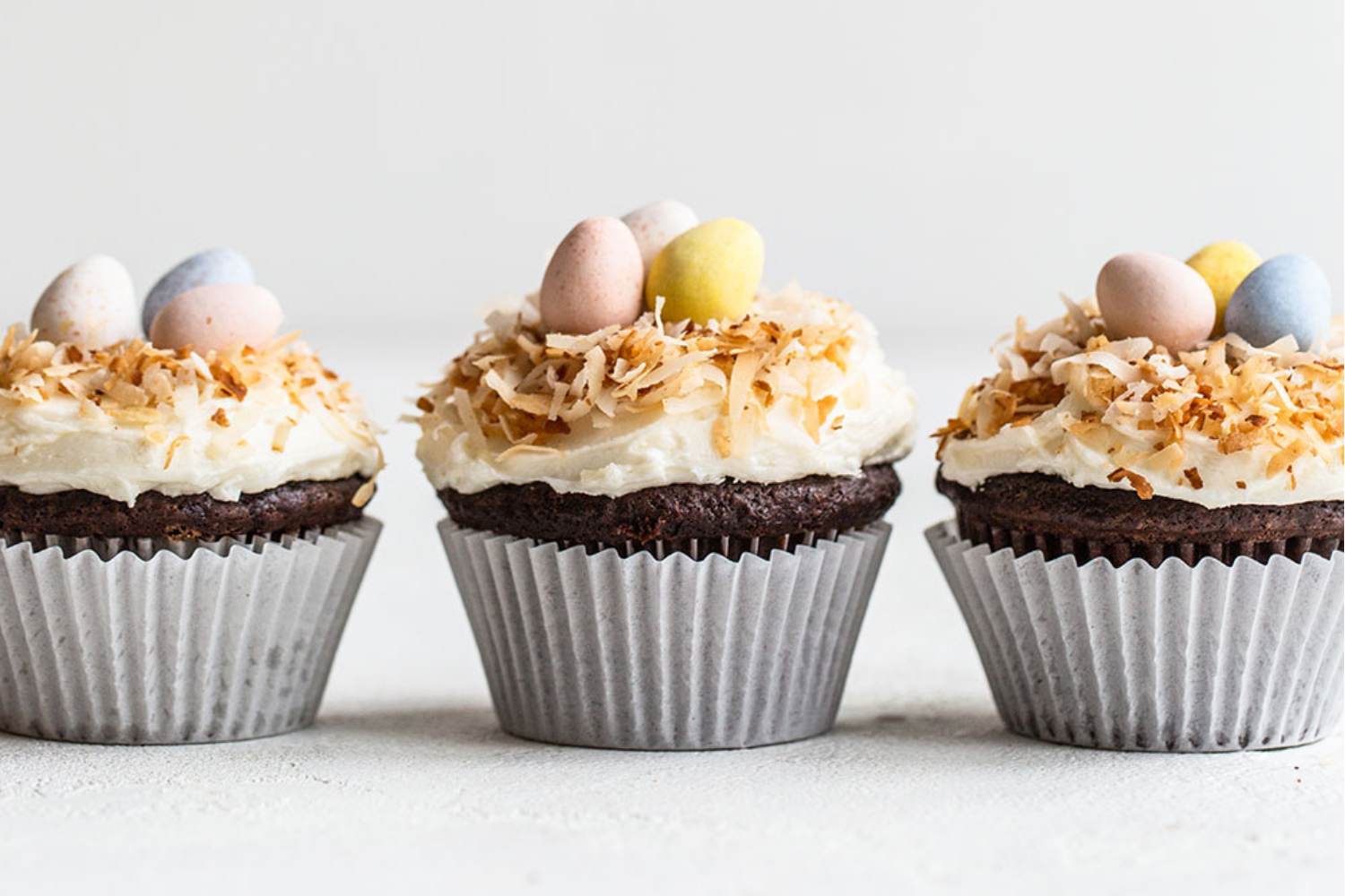 Drie afgewerkte chocolade-kokoscupcakes op een rij, gegarneerd met kokosvlokken en klaar om te serveren als heerlijke traktatie.