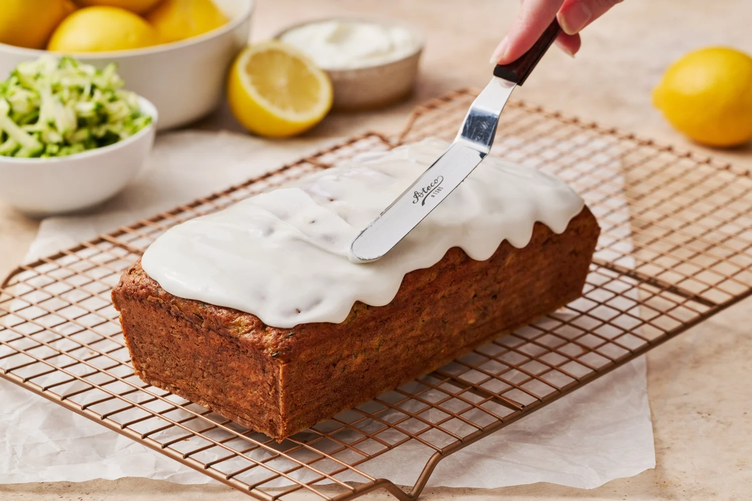 Volledige courgettecake die wordt geglazuurd met een citroenglazuur, met behulp van een offset spatel voor een gelijkmatige afwerking..de volledige cake van courgettebrood die wordt geglazuurd met een citroenglazuur, met behulp van een offset spatel.