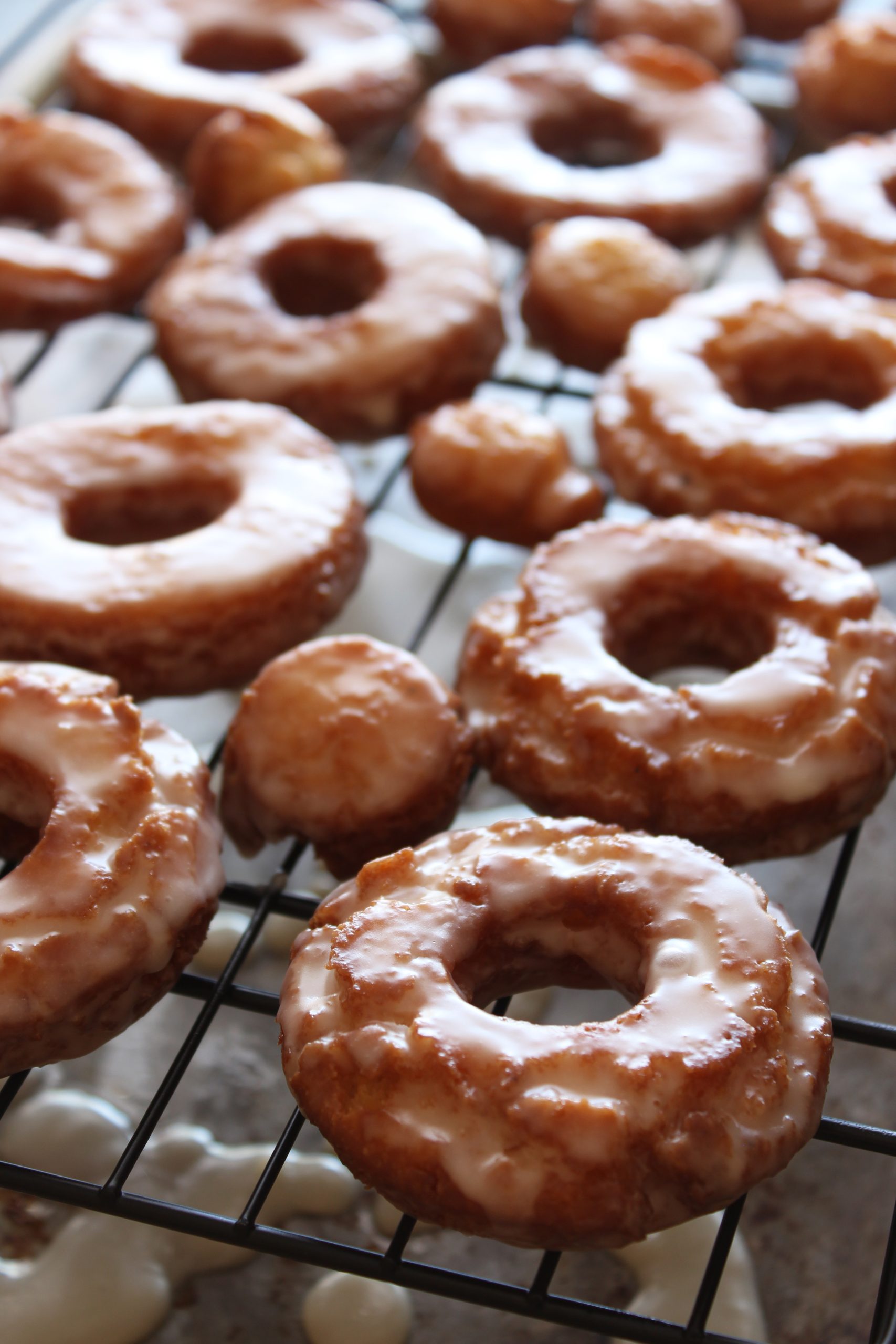 Verse oud-Hollandse zure room donuts, geplaatst op een ovenrek om te drogen na het glazuren, perfect voor bakkerij- en donutfotografie.