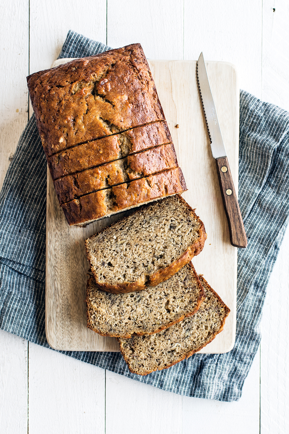 Bananenbrood wordt gesneden op een houten snijplank, met een zachte en vochtige binnenkant en een goudbruine korst.