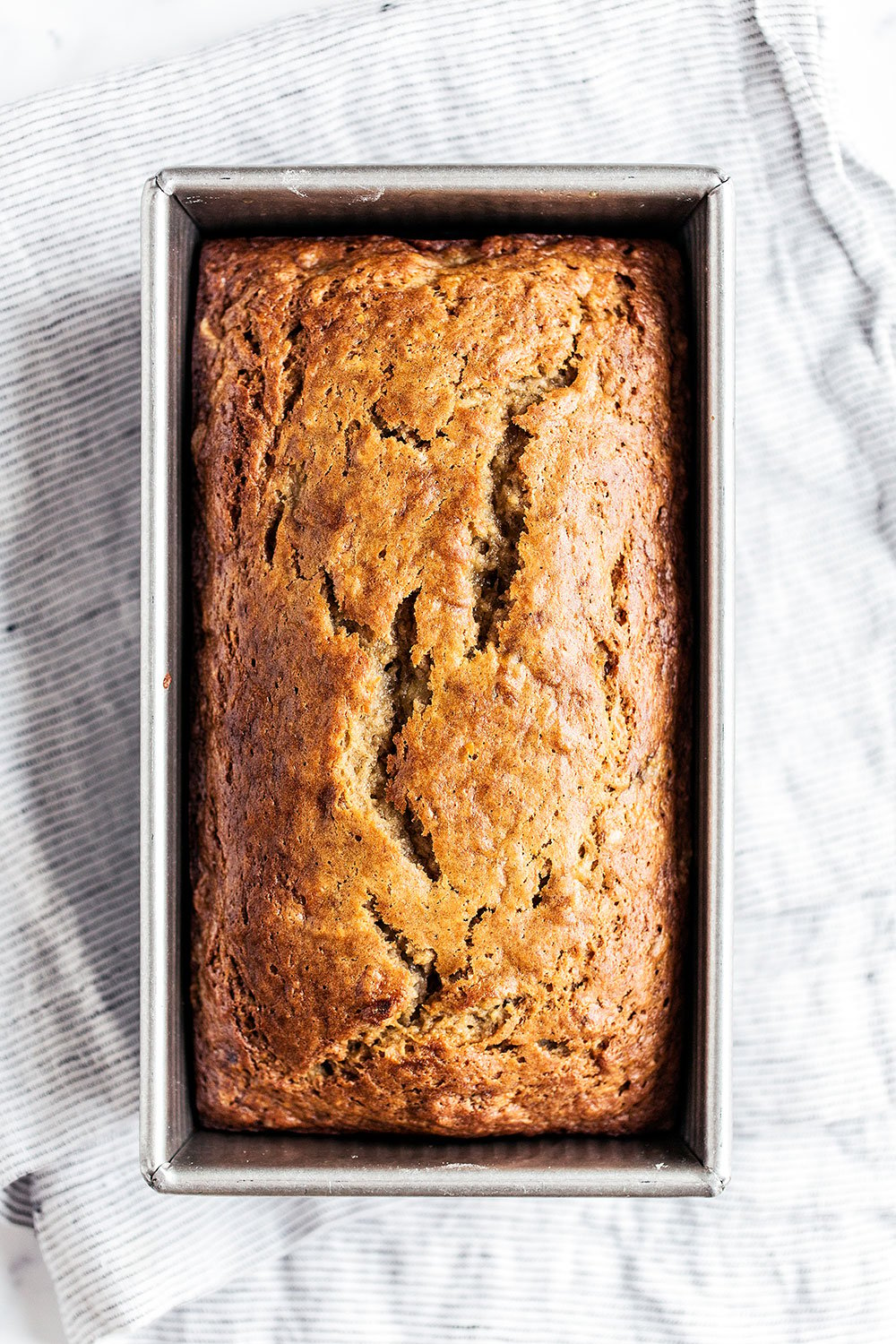 Volledig bananenbrood dat afkoelt in zijn metalen bakvorm, met een goudbruine korst en een zachte binnenkant