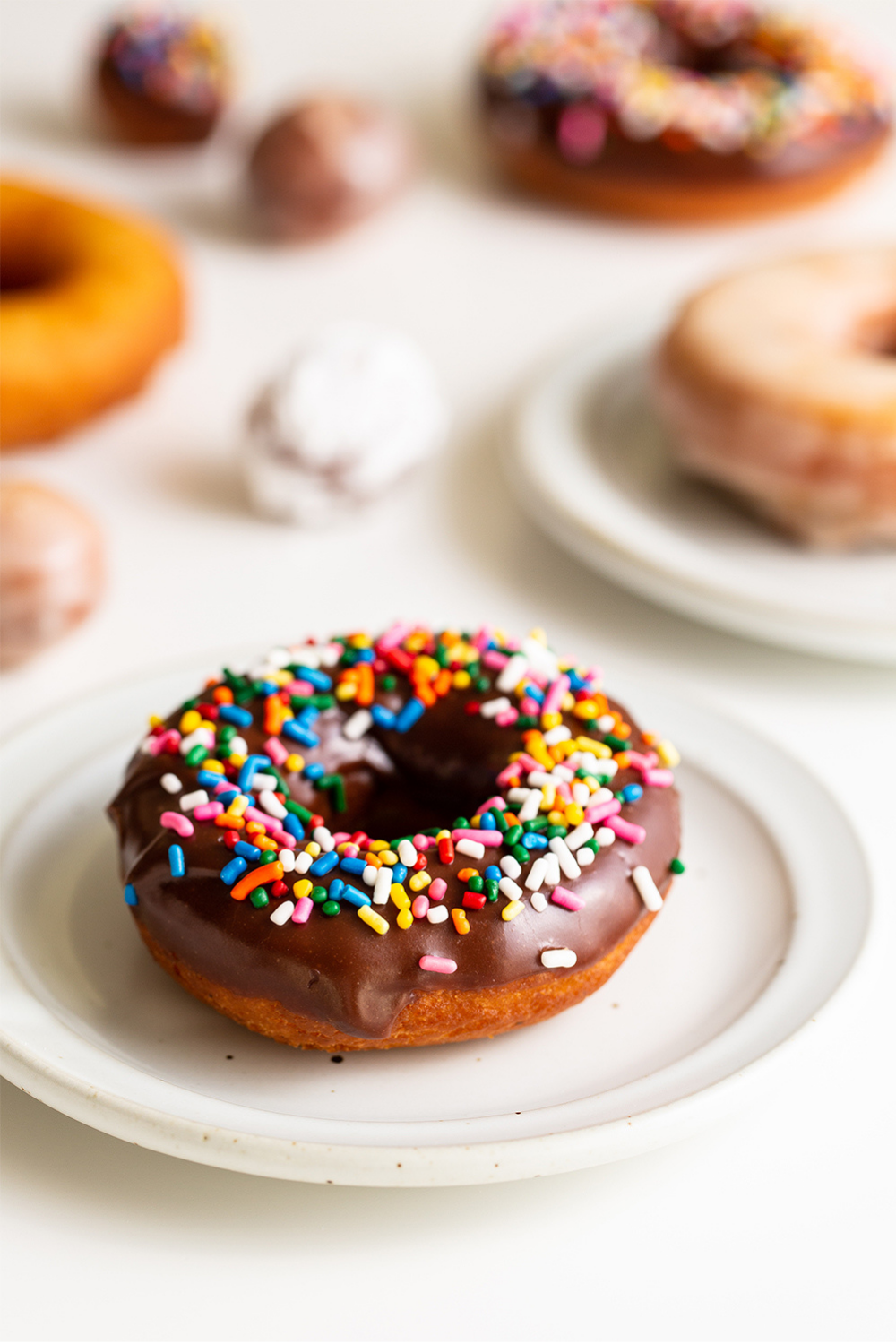 Een chocolade-gedoopte donut met kleurrijke sprinkles op een bord, klaar om te serveren, perfect voor dessert- en bakkerijfotografie.