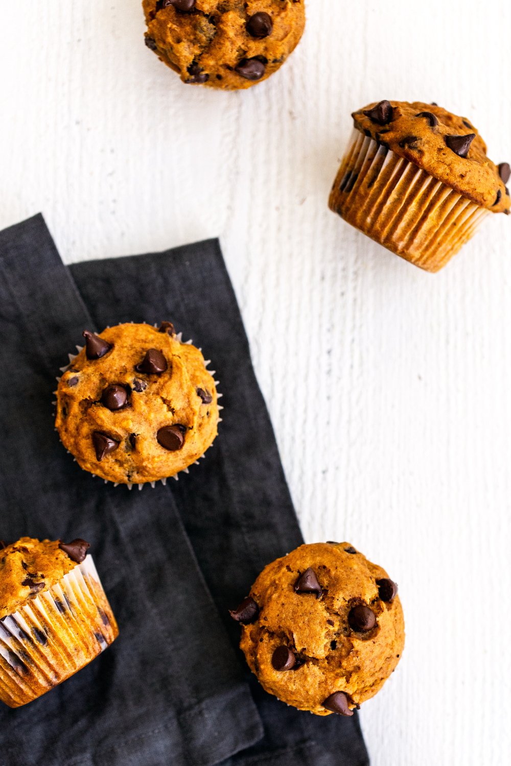 Pompoen chocolade chips muffins op een witte achtergrond, met een zwart servet, klaar om te serveren, ideaal voor herfst- en bakkerijfotografie.