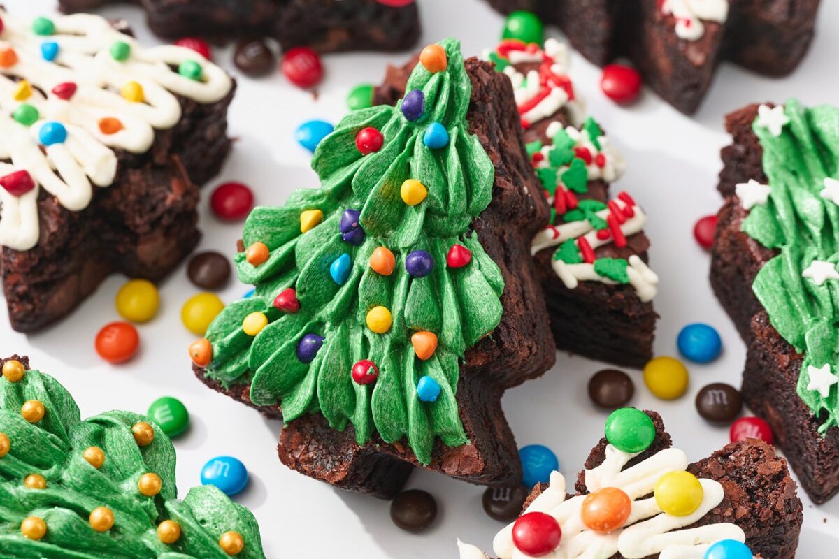 Een brownie in de vorm van een kerstboom, bedekt met groene botercrème en regenboogsprinkles, perfect voor feestdagen- en bakkerijfotografie.