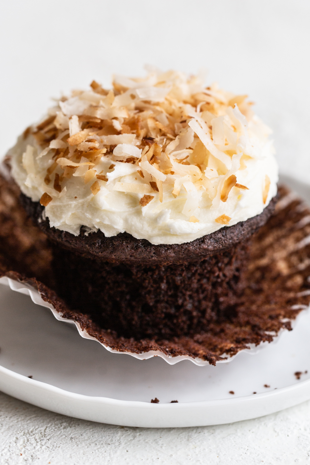 Chocolade kokos cupcake waarvan de wrapper wordt verwijderd, met een romige kokos-topping en een rijke chocoladesmaak.