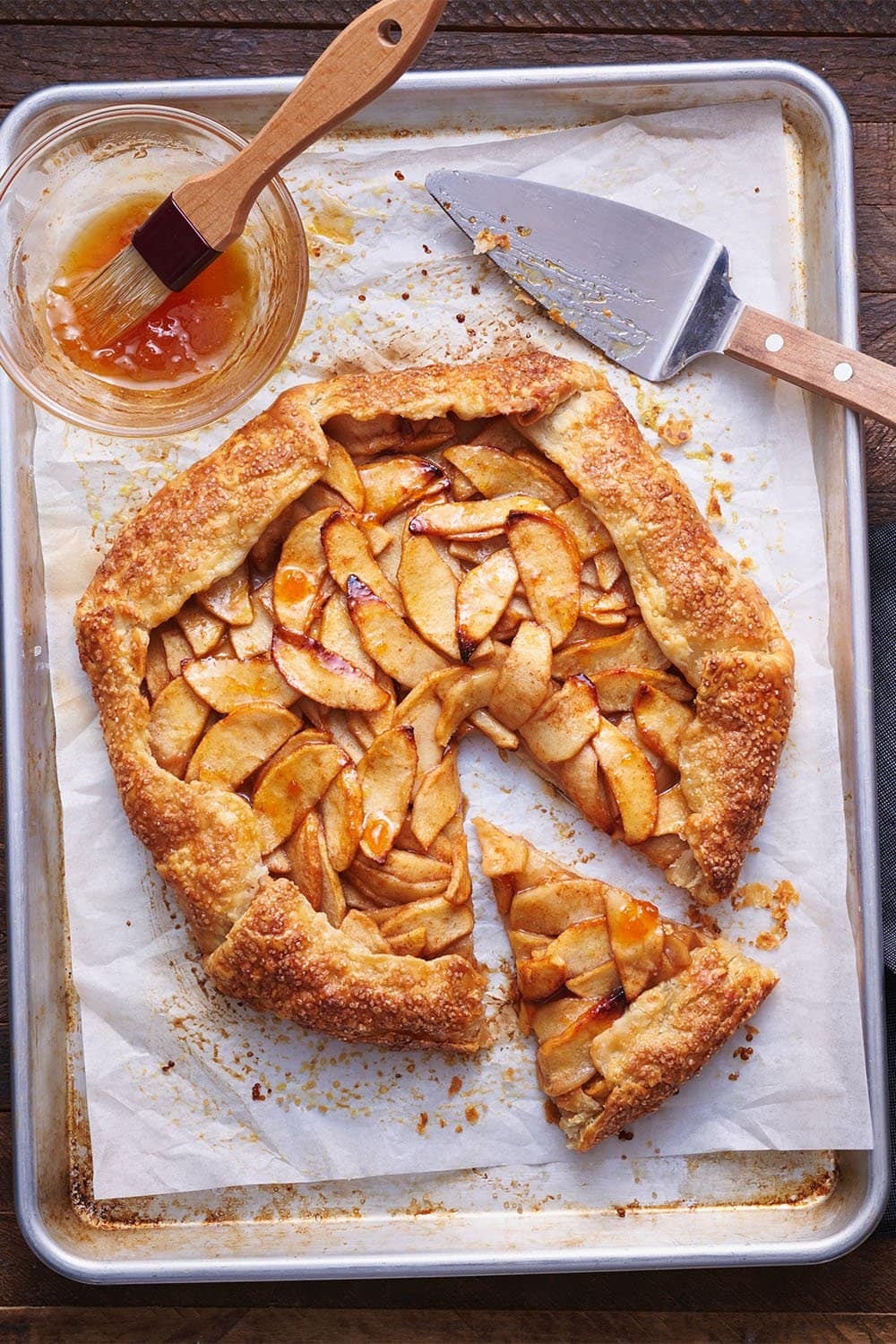 Zelfgemaakte rustieke apple galette op een bakpan met bakpapier, bedekt met abrikozenjam voor een mooie glans