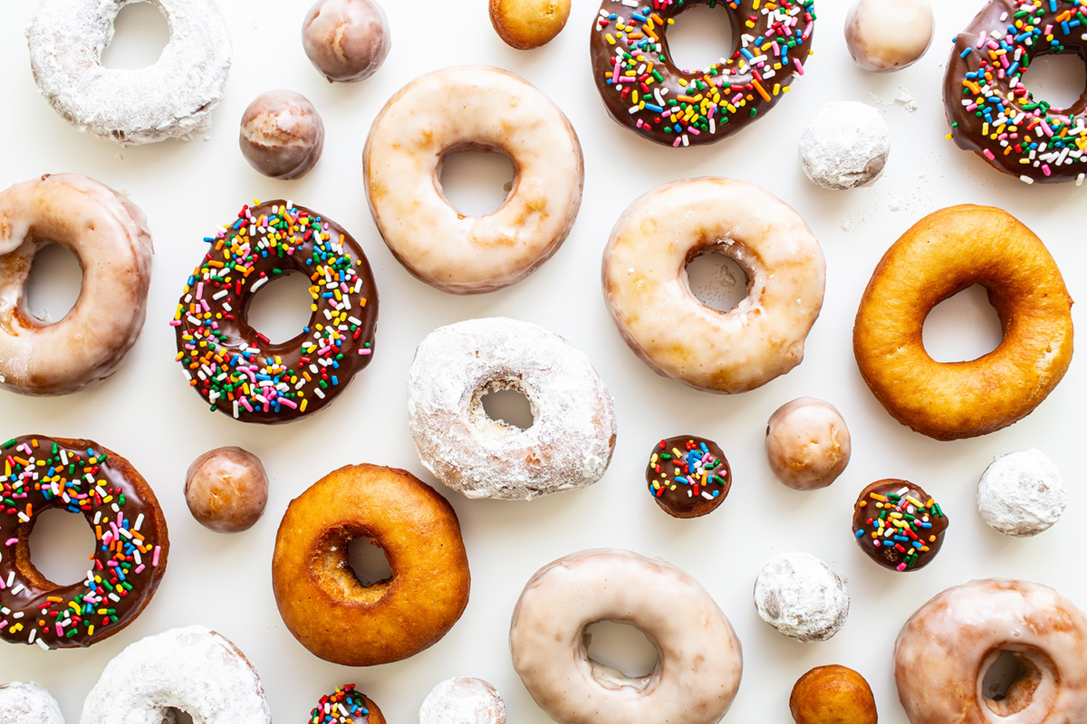 Een dozijn verse donuts op een witte achtergrond, met enkele donutgaten verspreid, perfect voor food fotografie en bakkerijpromotie.