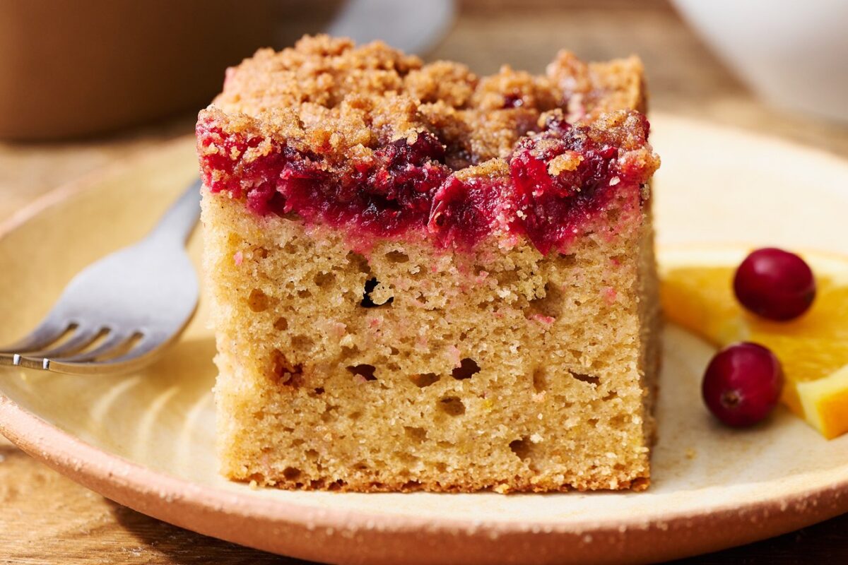 Een heerlijke plak cranberry-sinaasappel koffie cake, perfect gepresenteerd op een wit bord, klaar om geserveerd te worden.