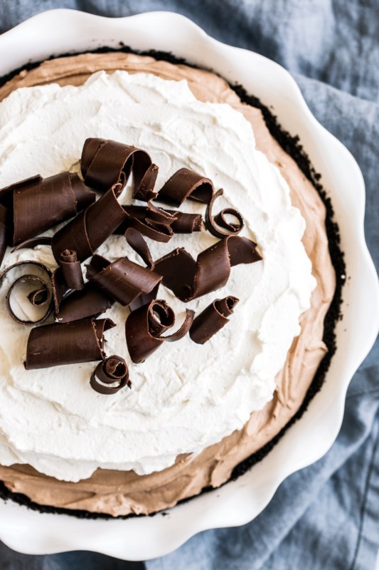 Franse Zijde Taart, bedekt met romige slagroom en decadente chocoladeslierten, gepresenteerd in een elegante keramische taartpan.