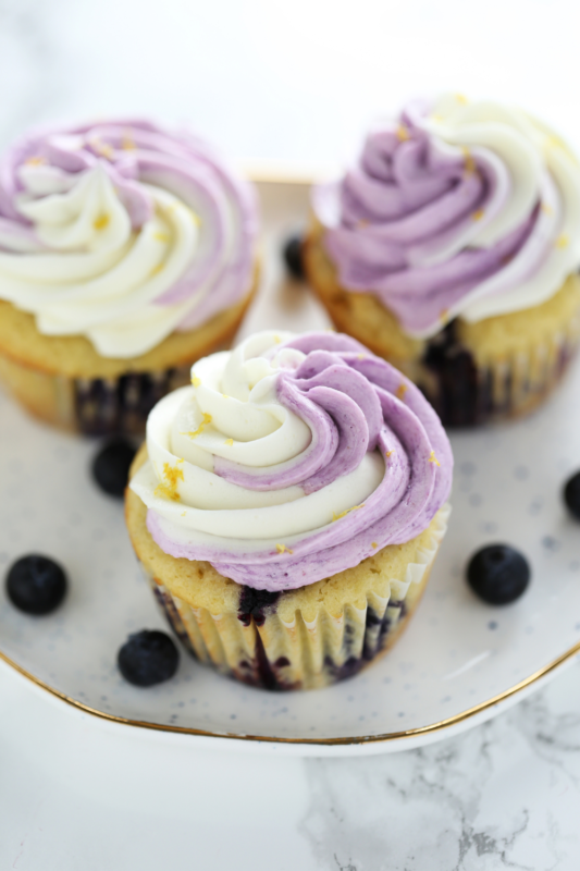 Three lemon blueberry cupcakes topped with creamy buttercream frosting and a sprinkle of fresh lemon zest, perfect for dessert and bakery photography.