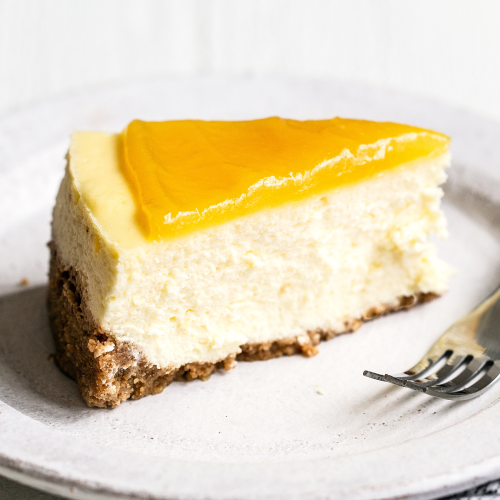 Een plak cheesecake bedekt met romige citroencurd, op een bord met een vork, ideaal voor dessert- en bakkerijfotografie.