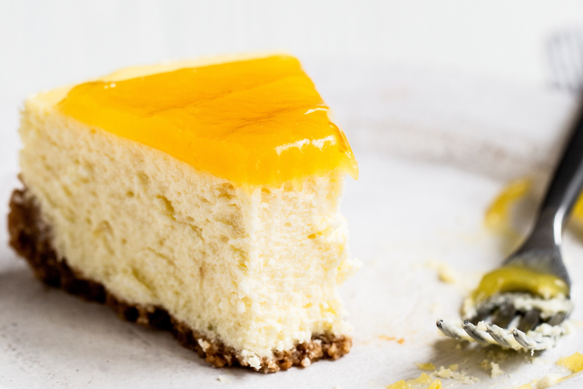 Een plak lemon cheesecake op een bord, met een vork en een hap eruit genomen, perfect voor dessert- en bakkerijfotografie.