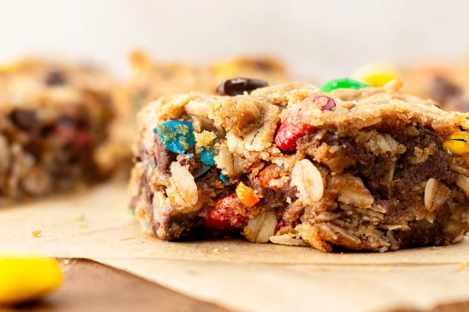 Een plak van monster cookie bar met een hap eruit, gevuld met chocolade, noten en M&M's, ideaal voor een lekkere snack.