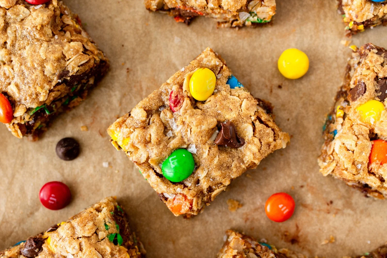 Plakjes monster cookie bars verspreid over bruin bakpapier, met kleurrijke M&M's ertussen, klaar om te serveren als een heerlijke traktati