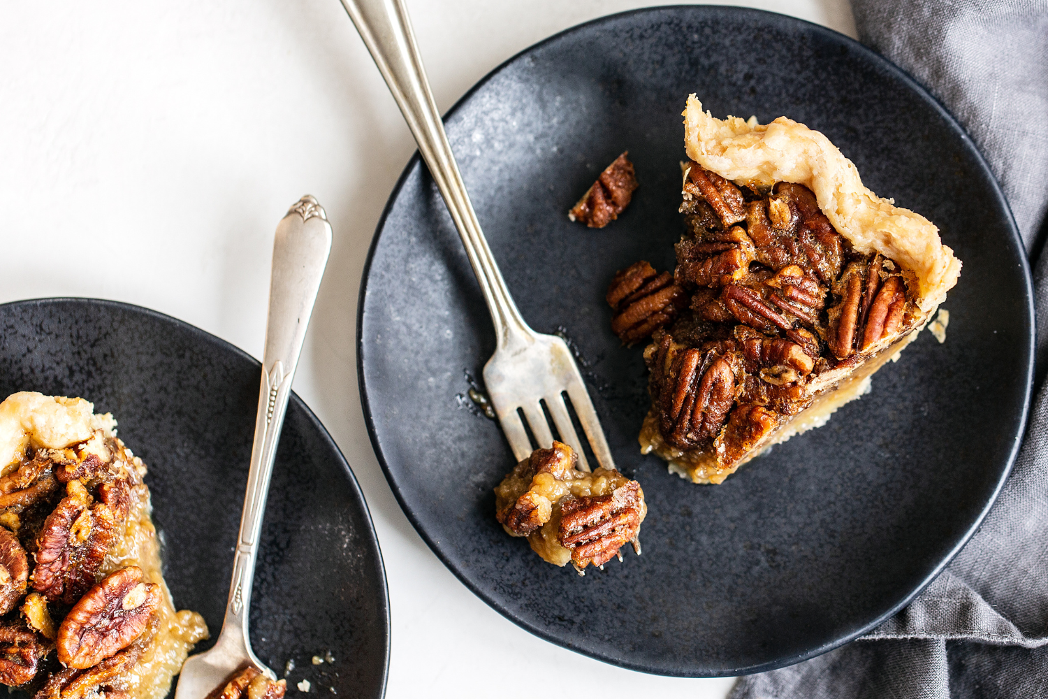 Smakelijke plakken pecantaart op elegante zwarte borden, geserveerd met vorken en servetten, klaar om van te genieten.