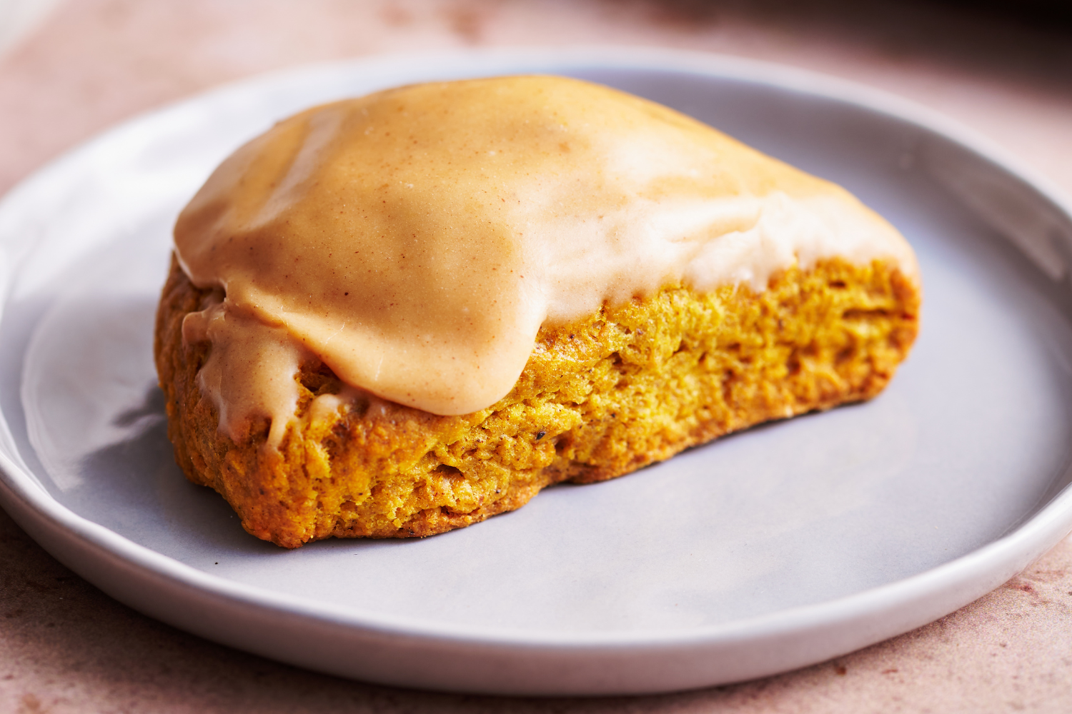 glazuurde pompoenkruidenscone op een bord.Glazuurde pompoenkruidenscone op een bord, een perfecte combinatie van herfstsmaken en zoete topping.