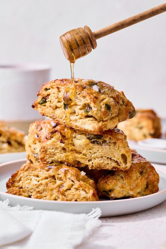 Honey being drizzled over a stack of savory shallot, jalapeño, goat cheese, and honey scones, perfect for dessert and recipe photography.