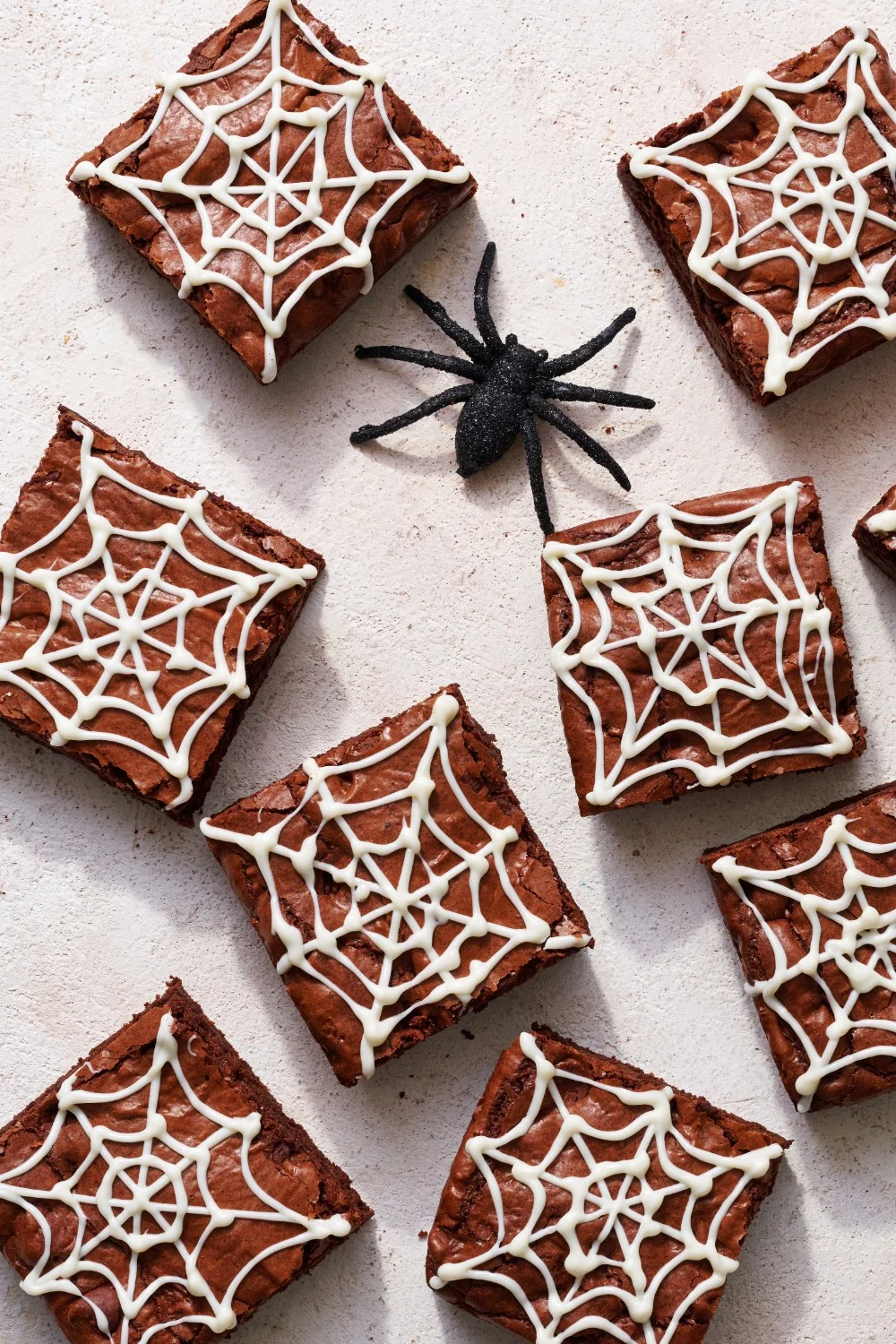 Verschillende brownies op een witte achtergrond, versierd met een plastic spin voor een extra griezelige uitstraling, perfect voor Halloween.