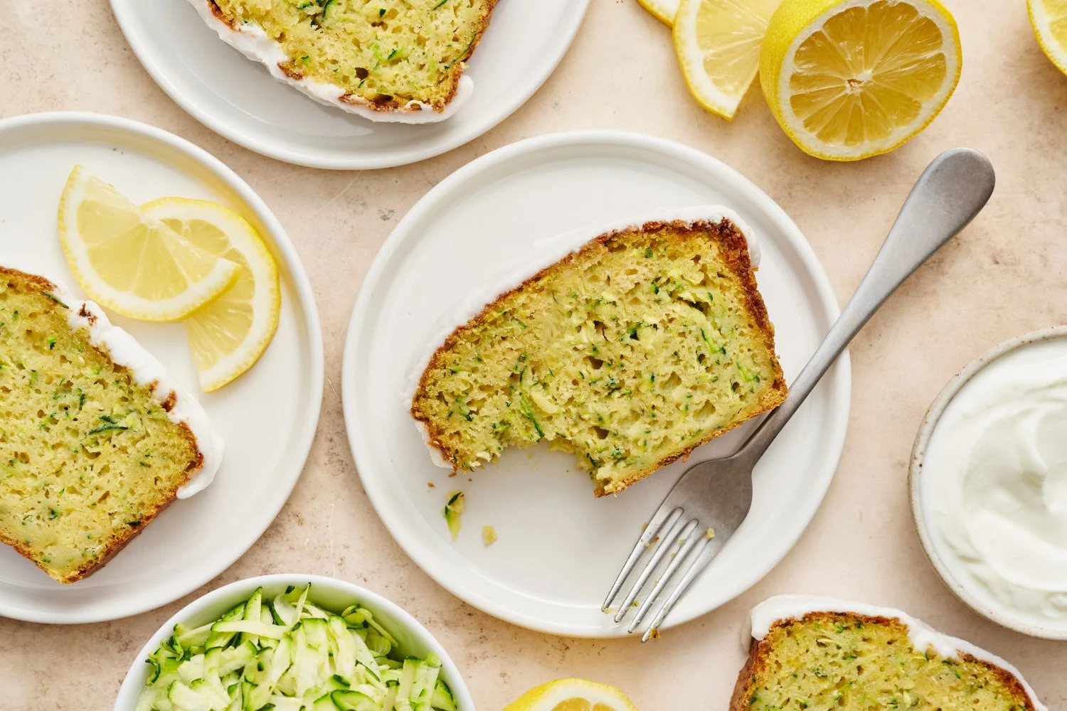 Plakken citroen-yoghurt courgettebrood op een bord met vorken, met een plak waar een hap uit is genomen, klaar om te serveren als een verfrissende traktatie.